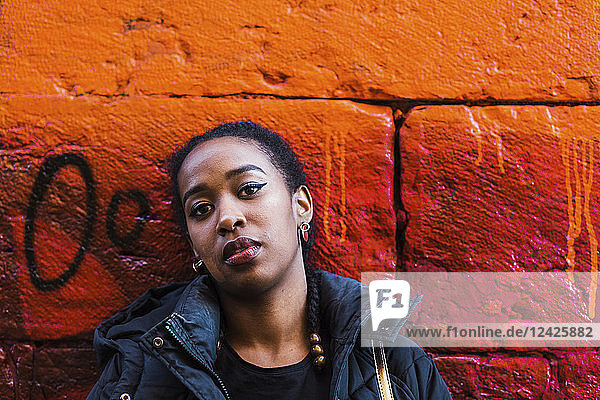 Ernste junge Frau lehnt an einer orangefarbenen Wand