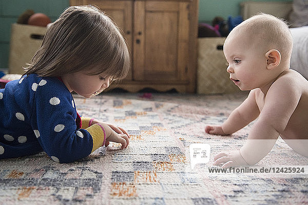 Schwestern (12-17 Monate  2-3) spielen auf dem Teppich