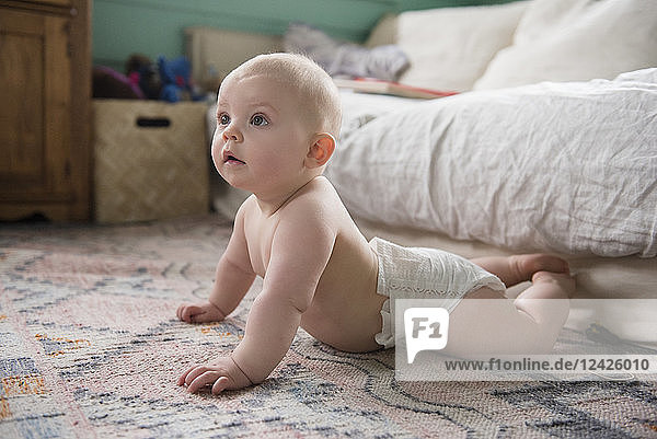 Kleines Mädchen (12-17 Monate) auf dem Teppich neben dem Sofa