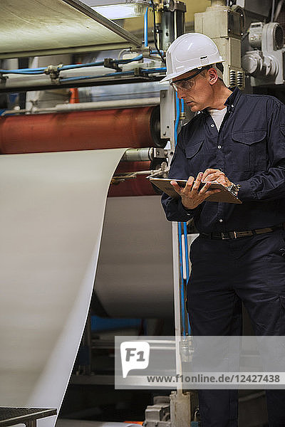 Factory worker writing on clipboard in factory