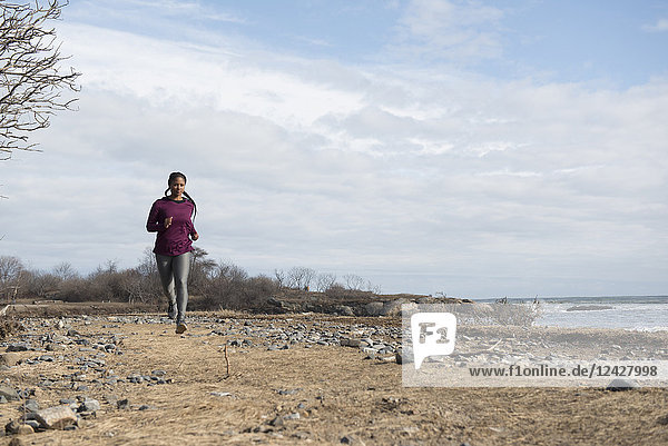 Front view of single woman trail running along coast of Maine  USA