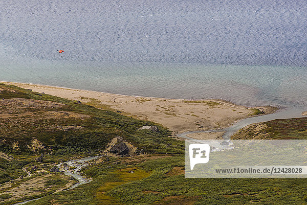 Distant view of person paragliding after base jumping from the top of Ulamertorsuaq 1000m high granite tower in the Tasermiut Fjord South Greenland