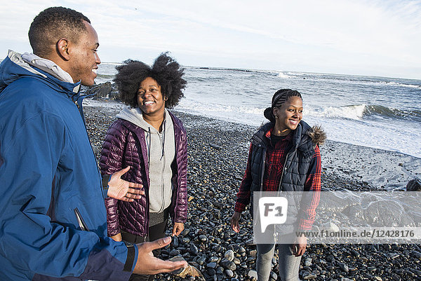 Drei lächelnde afroamerikanische Menschen stehen am Kiesstrand und unterhalten sich
