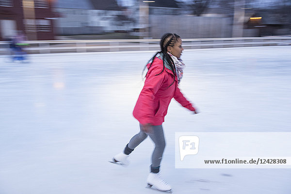 Seitenansicht einer einzelnen afroamerikanischen Frau mit Jacke beim Schlittschuhlaufen auf einer Eisbahn