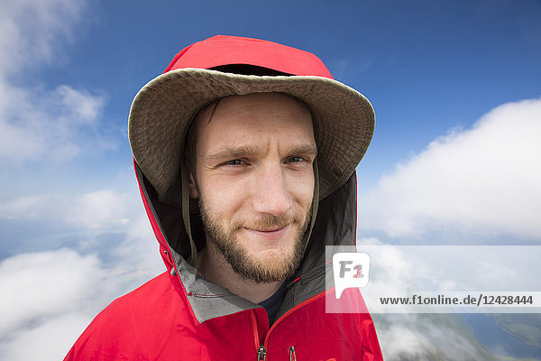 Kopf-Schulter-Porträt eines Wanderers in Kapuzenjacke und Hut in den Bergen