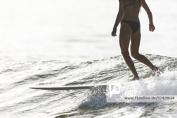 Tiefschnittaufnahme einer Frau im Bikini beim Longboard-Surfen im Meer