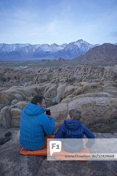 Vater und Sohn sitzen in der Alabama Hills Recreation Area mit den Sierra Nevada Mountains im Hintergrund  Lone Pine  Kalifornien  USA