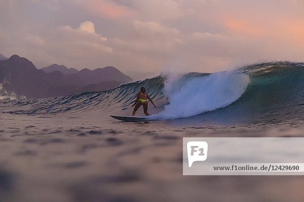 Rückansicht einer Surferin im Bikini auf einer Welle bei Sonnenuntergang