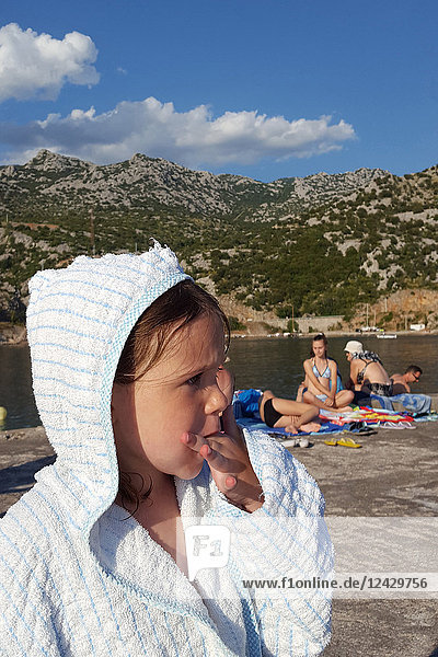Kopf- und Schulteraufnahme eines Mädchens im Bademantel  das nach dem Schwimmen im See einen Snack isst