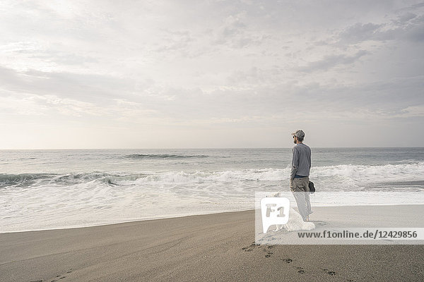 Mann mit Hund am Strand stehend und mit Blick auf das Meer