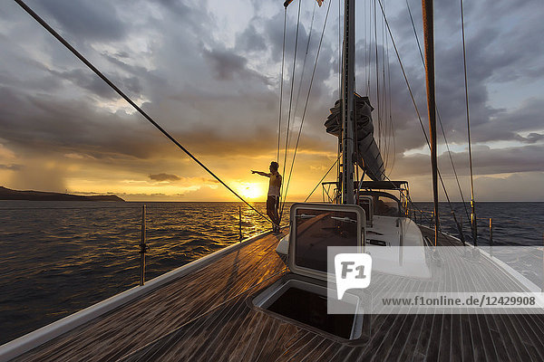 Distant view of single man standing on deck of large yacht and pointing at sunset on horizon  Lombok  Indonesia