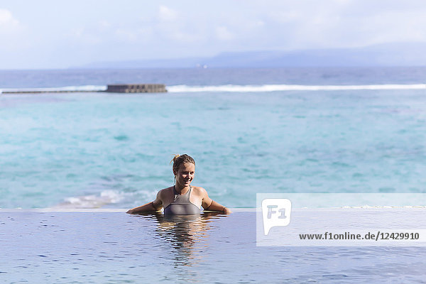Vorderansicht einer lächelnden jungen Frau im Badeanzug im Schwimmbad mit Blick auf das Meer