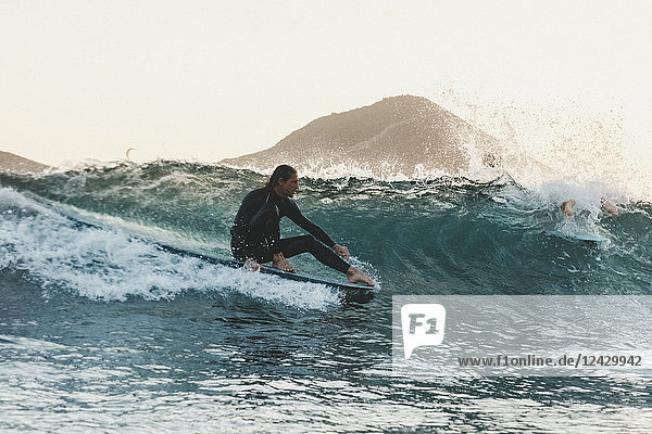 Seitenansicht von Longboard-Surfer in Neoprenanzug Reiten Welle im Meer bei Sonnenuntergang Schuss