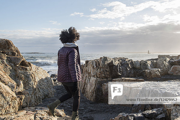 Rear view shot of African American woman walking on rocky coastline  Kittery  Maine  USA