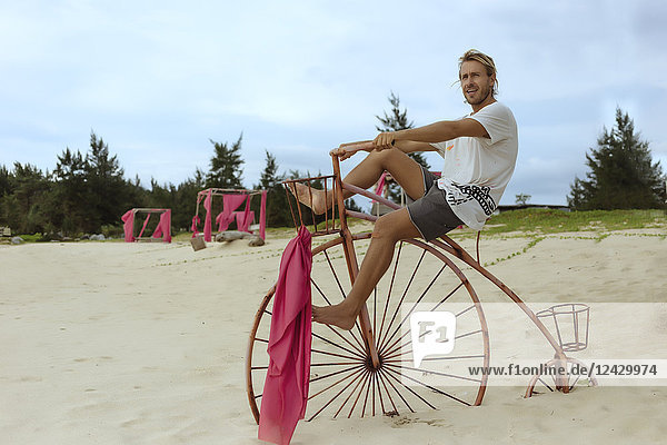 Totale Aufnahme eines jungen Mannes  der auf einem hölzernen  dekorativen Penny-Farthing-Fahrrad am Strand sitzt  Banda Aceh  Sumatra  Indonesien