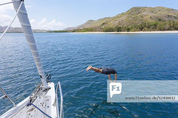 Totale Aufnahme eines Mannes in der Luft  der vom Boot aus ins Wasser taucht  Lombok  Indonesien