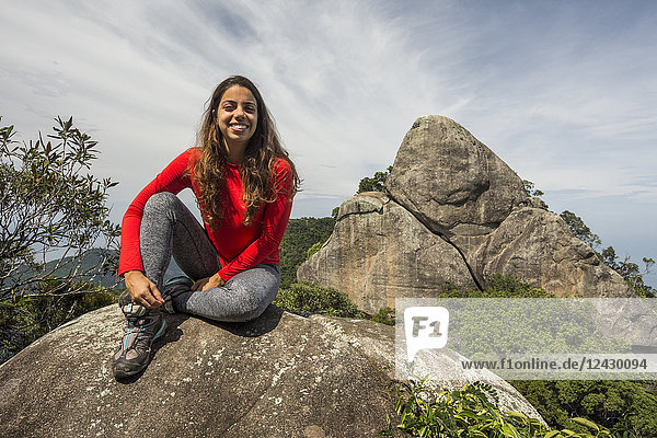 Front view of smiling woman sitting on rock in natural setting  Tijuca Forest  Rio de Janeiro  Brazil