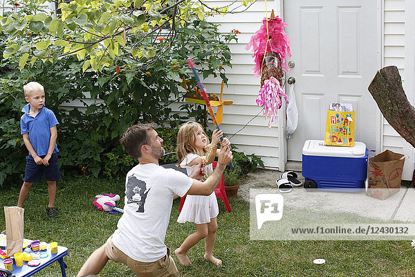 Mid adult father playing with little daughter during birthday party in front or back yard