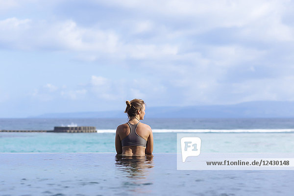 Rückansicht einer jungen Frau im Badeanzug im Schwimmbad mit Blick auf das Meer
