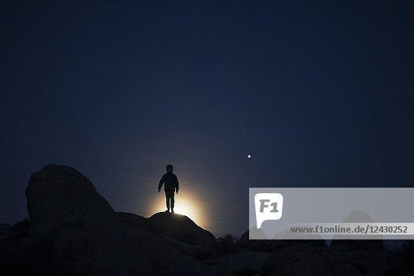 Silhouette of boy standing on rock formation at night