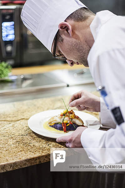 A Caucasian male chef putting the finishing touches on a plate of fish in a commercial kitchen.