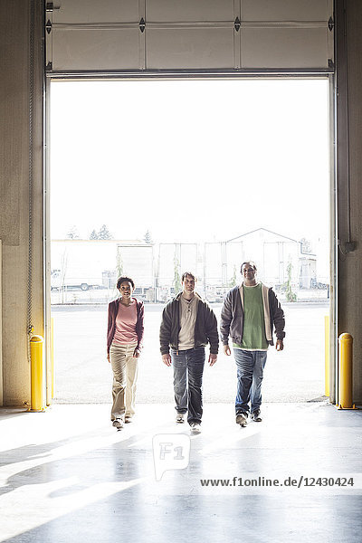 Three employees walking through the loading dock door of a distribution warehouse.