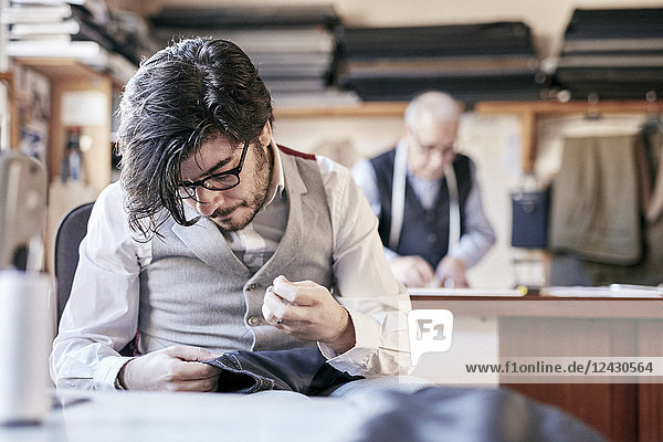 Tailor with measuring tape around neck working with material at bench