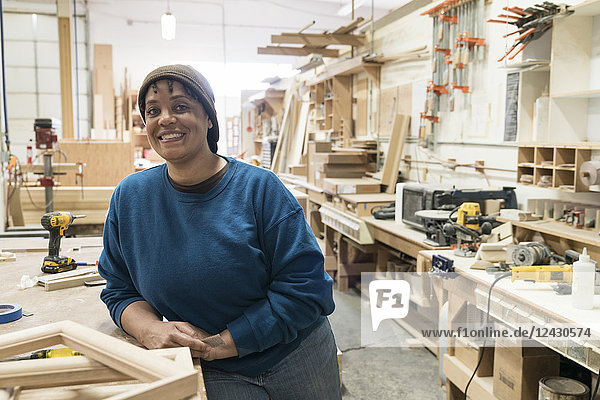 Portrait of a Black woman carpenter in a large woodworking shop.