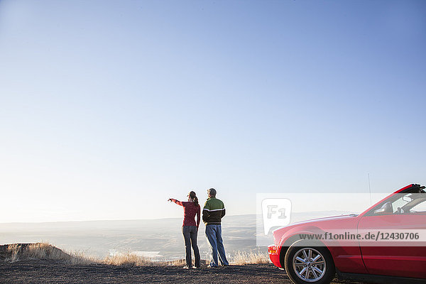 A young Caucasian couple admires the view at a rest stop in Eastern Washington  USA while on a road trip with their convertible sports car.