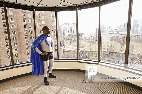 Ein Superheld aus dem Büro eines schwarzen Geschäftsmannes steht an einem Bürofenster und sinniert über seinen nächsten geschäftlichen Schritt.