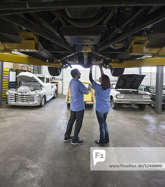 Männliche und weibliche Mechaniker  die in einer Reparaturwerkstatt an der Unterseite eines Autos an einem Aufzug arbeiten.