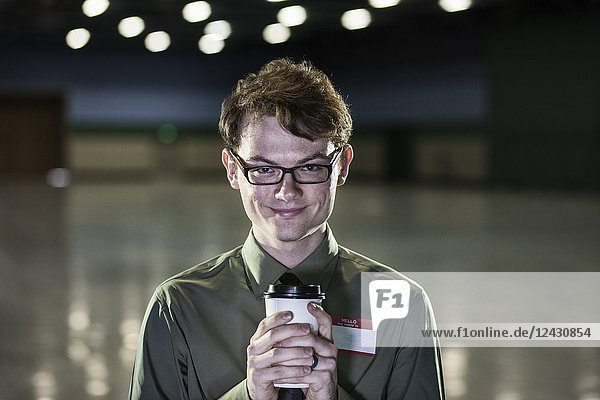 A young hip businessman standing in a dimly lit and dark exhibition area in a convention centre.