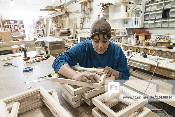 Eine schwarze Schreinerin  die in einer großen Holzwerkstatt an einem Schrankprojekt arbeitet.