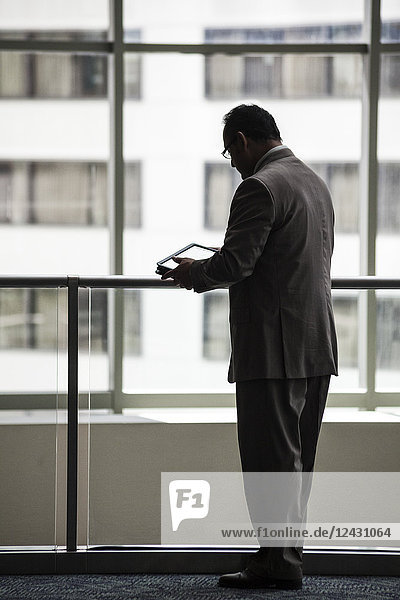 Ein hispanischer Geschäftsmann mit einem Notebook-Computer  während er vor einem Fenster in der Lobby eines Kongresszentrums steht.