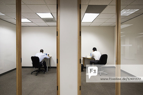 Ein Blick auf zwei Geschäftsleute  die auf gegenüberliegenden Seiten einer Wand in zwei verschiedenen Büroräumen arbeiten.