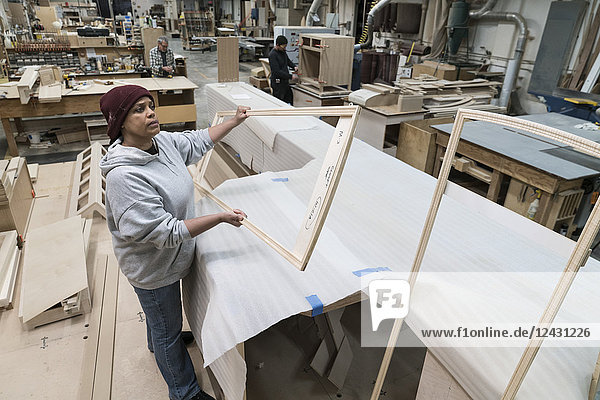 A Black woman carpenter working on a cabinet project in a large woodworking shop.