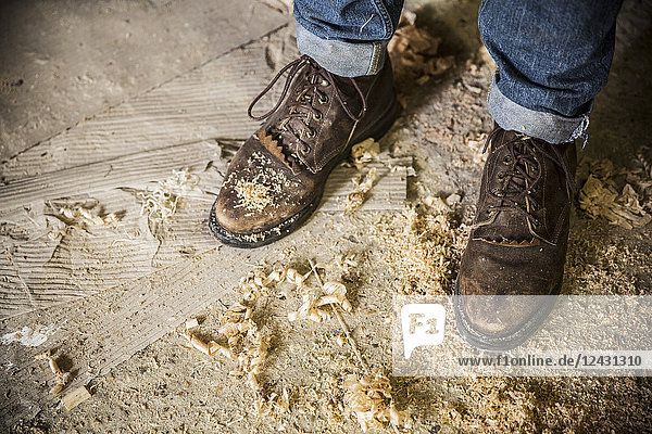 Schrägansicht eines Mannes in Jeans und braunen Lederstiefeln  der in einer Werkstatt steht  Holzspäne auf dem Boden.