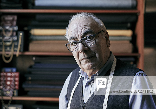 Porträt eines älteren Schneiders mit einem Maßband um den Hals  in seinem Arbeitszimmer.