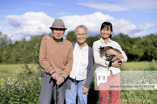 Lächelnde Frau hält eine graue Katze  die im Freien steht  mit einem älteren Mann und einer älteren Frau  die in die Kamera lächeln.