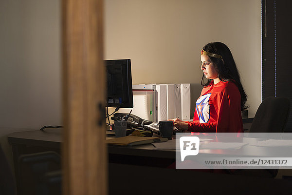 An Hispanic businesswoman office super hero at her office computer