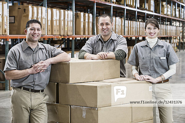 Ein Teamporträt von drei gemischtrassigen uniformierten Lagerarbeitern in einem großen Vertriebslager  umgeben von verpackten Produkten.