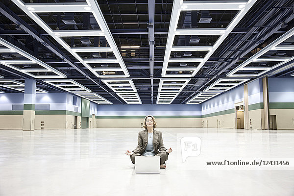 Eine Geschäftsfrau in einer Yoga-Pose mit einem Laptop-Computer in der Mitte einer Kongresszentrum-Arena.