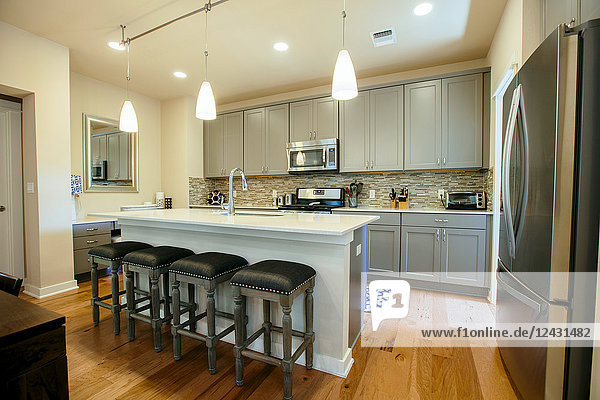Moderne Wohnküche mit grün-grauen Einbauschränken  einer Kücheninsel mit hohen Barhockern und Holzfußboden.