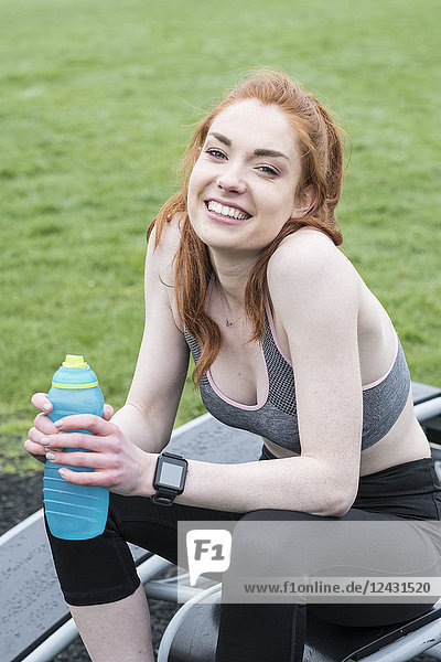 Lächelnde junge Frau mit langen roten Haaren in Sportkleidung  die im Freien Sport treibt und in die Kamera schaut.
