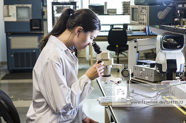 A Caucasian female technician using a microscope to examine a part in a technical research and development site.