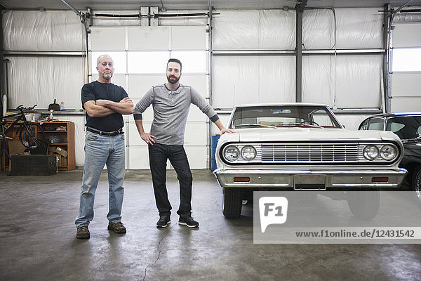 A portrait of a Caucasian senior car mechanic and his son in their classic car repair shop.