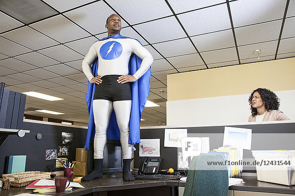 A black businessman office super hero stands on his cubicle desk ready for action.