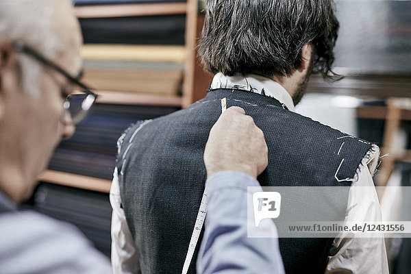 Schneider  der ein Maßband an einer Anzugjacke verwendet und das Kleidungsstück einem Kunden anpasst