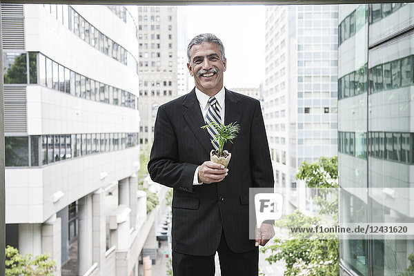 A businessman holding a small plant while standing next to a large convention centre window.