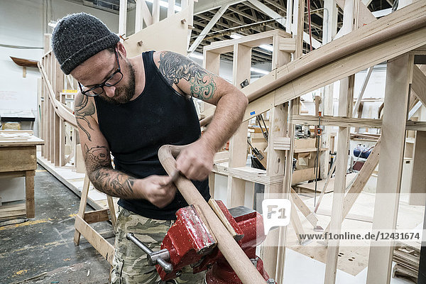 Kaukasischer Zimmermann  der in einer großen Holzwerkstatt an einem Wendeltreppengeländer arbeitet.